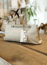 Sobre de cuero color crema con textura tipo piel de cocodrilo, herraje metálico color peltre y cierre con broche imantado.