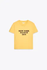 Camiseta amarilla de algodón con cuello redondo, manga corta y estampado marrón con el texto "New York Fluxus 1970".