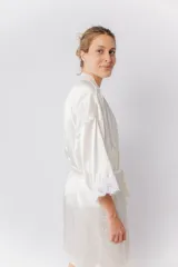 Bata kimono de satén elastizado color blanco, con mangas al codo terminadas en puntilla y largo por encima de la rodilla. Incluye lazo de satén para ajustar en la cintura.