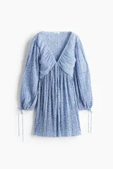 Vestido corto azul con estampado floral blanco, escote en V pronunciado con fruncido central, mangas globo largas con lazos ajustables en los puños y falda corta plisada.