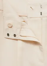 Pantalón de vestir color crema, de corte recto y largo, con pinzas delanteras, bolsillos laterales y trabillas.