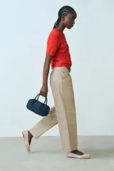 Pantalón color beige de corte holgado en sarga de algodón. Modelo de tiro alto con cierre, pretina prolongada con botón oculto y corchetes, bolsillos al bies y bolsillos insertados atrás. Piernas rectas con pinzas y pliegues adelante y atrás.