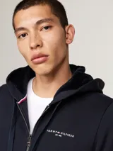 Buzo azul marino con capucha, cierre de cremallera frontal, bolsillos tipo canguro y logo de Tommy Hilfiger bordado en el pecho.