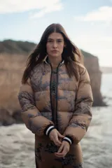 Campera puffer color camel con estampado de paisaje en azul marino, cuello y puños tejidos con rayas blancas y negras. Impermeable.