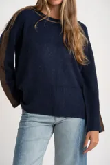 Sweater de punto azul marino con calce oversize. Presenta un detalle de franja vertical color marrón en la parte exterior de ambas mangas y un ribete fino dorado en el escote redondo.