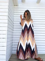 Vestido camisero largo con estampado chevron en tonos chocolate, beige, negro y crudo. Tiene cuello camisero, mangas largas y cierre frontal con botones. Presenta aberturas laterales en el ruedo.