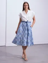 Vestido midi camisero de algodón con estampado floral en tonos azules y blancos. Tiene cuello solapado, cierre frontal con botones, manga corta, cintura elastizada con lazo de ajuste y bolsillos laterales.