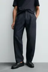 Pantalón de denim azul oscuro, corte wide fit, largo cropped, con pliegues frontales, bolsillos laterales y traseros asimétricos. Cierre frontal con cremallera y gancho metálico oculto.