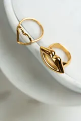 Anillo dorado con forma de labios y corazón, fabricado en acero quirúrgico.