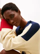 Cárdigan de punto color crema, con cuello en V, cierre con botones y corte amplio. Presenta detalles en azul marino en los hombros y en el borde del cuello, y detalles en rojo en los puños y en el ruedo. Logo de Tommy Hilfiger bordado en el pecho.