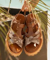 Sandalias bajas de cuero vacuno color beige con tiras cruzadas plateadas y hebilla lateral. Suela doble de goma deportiva con altura de 3cm adelante y 5,5cm atrás.