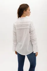 Camisa blanca de algodón con volados en el pecho y cuello, botones nacarados y mangas largas con puños elásticos.