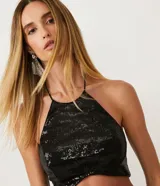 Blusa cropped de lentejuelas negras con cuello halter y espalda descubierta.