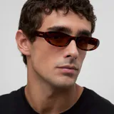 Lentes de sol con montura ovalada y ligeramente plana, estilo ojo de gato, en color carey (marrón jaspeado). Los lentes son polarizados de color marrón.