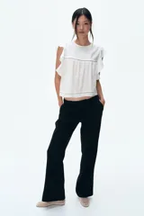Pantalón negro de corte sastrero con cintura estándar, cierre y botón. Tiene bolsillos al bies en la parte delantera y bolsillos insertados decorativos en la parte trasera. Las piernas son acampanadas.