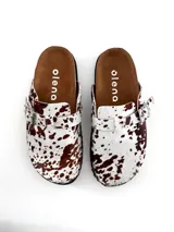 Zuecos de cuero con estampado de vaca en blanco y marrón, con hebilla lateral ajustable.