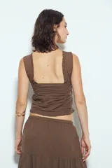 Top corto color marrón, con escote cuadrado y breteles anchos con volados. Presenta frunces horizontales en el torso y una hilera de botones nacarados en el centro frontal.