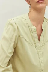 Camisa celeste de manga larga con cuello redondo y escote en V. Presenta detalles de pasamanería en el frente y las mangas, y botones forrados al tono. De corte fluido.