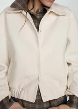 Chaqueta color crema de tejido de punto con terminación elástica, cuello camisero, diseño oversize, manga larga y cierre frontal con botones a presión ocultos.