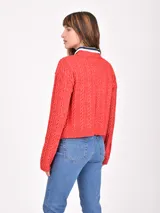 Buzo de tejido de punto trenzado color rojo, con cuello redondo y puños y ruedo acanalados. Se lleva sobre una camisa de cuello a rayas blancas y azul marino.