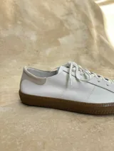 Zapatillas bajas de cuero negro con cordones y suela de goma color caramelo.