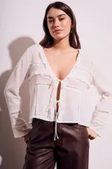 Blusa blanca de algodón con escote en V, mangas largas con detalles de encaje y cierre frontal con lazos.