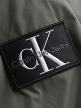 Campera bomber verde militar de poliéster reciclado, con cuello alto, puños y bajo elásticos. Cierre de cremallera, bolsillos ribeteados en la cintura y forro ligeramente acolchado. Logo de Calvin Klein en el pecho y la manga.