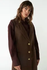 Chaleco largo color crema de lana fina sin mangas, con solapas y cierre frontal con tres botones. Presenta bolsillos ojal.