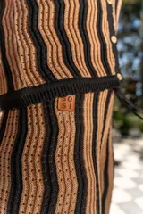 Conjunto tejido de dos piezas con rayas verticales en tonos marrón y negro. Incluye un chaleco sin mangas con botones y un pantalón de corte recto.