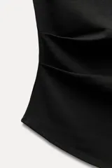 Musculosa negra con cuello barco, sin mangas, detalle de pliegues laterales y bajo asimétrico.