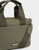 Cartera tipo tote color blanco hueso, con doble asa corta negra y correa larga negra regulable y desmontable. Tiene cierre superior, bolsillos laterales y tag de goma con el logo de la marca.