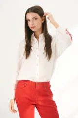 Camisa blanca de manga larga con bordados florales marrones en las mangas.
