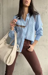 Camisa celeste de manga larga con cuello mao y cierre frontal con botones. Presenta detalles de broderie en el frente y mangas.