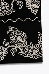 Pantalón culotte negro de lino y viscosa con bordados florales en el ruedo. Tiene tiro medio, cintura con trabillas, bolsillos laterales y cierre frontal con cremallera y botón.