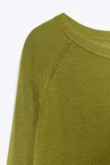 Jersey de punto color verde oliva, con cuello redondo y manga larga. Tiene bajo con aberturas laterales y acabados en rib.