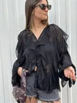 Blusa negra traslúcida con volados, mangas largas abullonadas y cierre frontal con botones.