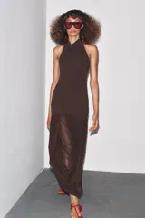 Vestido largo color marrón oscuro, con cuello halter que forma un drapeado en el busto. La parte superior es ajustada y la falda es larga con un panel inferior fruncido y drapeado en tela más liviana.