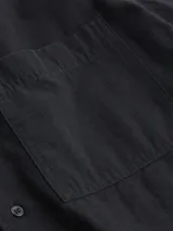 Camisa negra de manga corta con cuello cubano y bolsillo de parche en el pecho. Cierre frontal con botones y logo de la marca en el bolsillo.