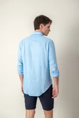Camisa celeste de lino con cuello clásico y manga larga. Presenta un pequeño logo bordado en el pecho.