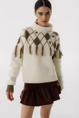 Sweater tejido de punto color crudo con cuello alto y diseño de rombos marrones con flecos.