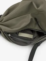 Bolso tipo macuto mediano color verde, confeccionado en poliéster. Tiene un compartimento principal con cierre de cremallera lateral y un bolsillo interior con cremallera. Cuenta con asa larga regulable y cinta a contraste a modo de estrangulador.