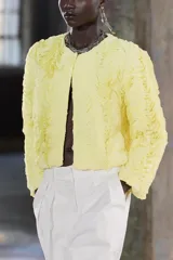 Chaqueta corta color amarillo pastel con textura de volantes, cuello redondo, manga larga y cierre frontal con botón a presión oculto.