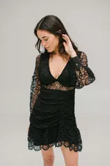 Vestido corto de encaje negro con escote en V, mangas largas abullonadas y falda con volados. Presenta cierre invisible en la espalda.