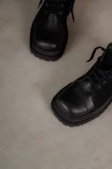 Borcegos negros de cuero charol, con punta cuadrada, cordones y suela track.