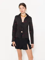 Camisa negra de poplin con bordado de chiles rojos, cierre frontal con lazos, broches decorativos dorados en el cuello y broches a presión dorados en los puños.