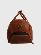 Bolso de viaje tipo maletín, fabricado en cuero natural color caramelo. Presenta dos asas superiores y una correa ajustable y desmontable. Cuenta con un compartimento principal con cierre, un bolsillo interior con cierre y un bolsillo lateral con cierre.