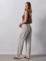Pantalón de lino a rayas verticales color beige y blanco, con pretina ancha elastizada, lazo de ajuste y bolsillos inclinados.