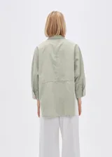 Camisa color verde claro, de corte holgado, con cuello clásico, cierre frontal con botones, mangas 3/4 y dos bolsillos de parche en el pecho.