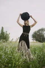 Vestido largo de crochet color negro, con cuello redondo y sin mangas. Presenta flecos de lurex color crudo en el ruedo.