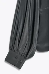 Camisa gris confeccionada en seda 100%, de cuello redondo y manga larga abullonada con puño. Cierre frontal con botones ocultos por solapa.